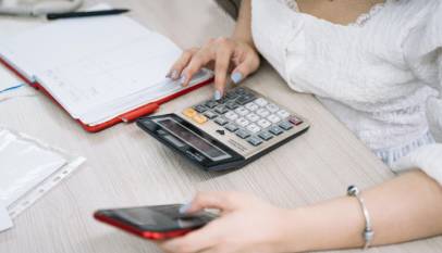 prestação de contas: imagem de uma mulher caucasiana segurando um celular e digitando em uma calculadora