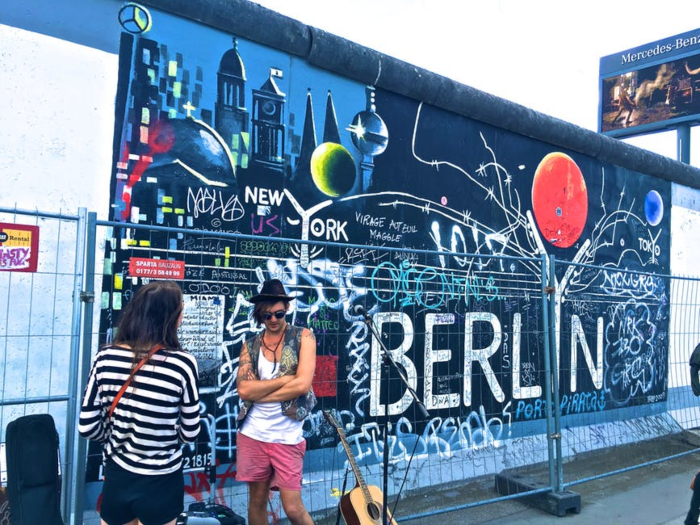 moça e homem estilosos conversando na frente de um muro com grafite de cidades
