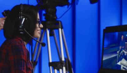 Qual o trabalho do produtor: imagem de uma mulher caucasiana acompanhando uma filmagem por uma tela de apoio