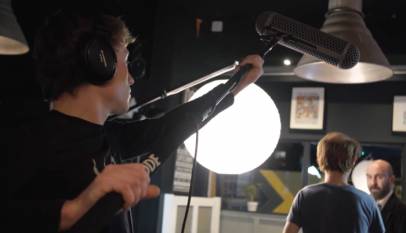 Imagem de um operador de boom segurando o microfone gravando uma conversa entre dois atores